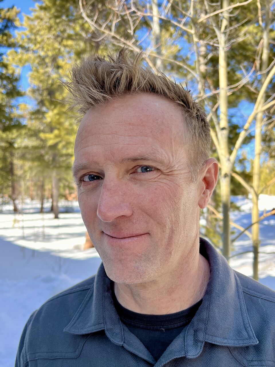 Luke Miller outdoors in winter, with snow and aspen trees behind him